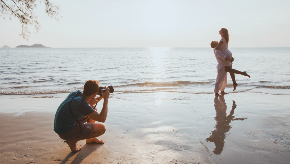 Newly married couple having wedding photos taken on beach abroad